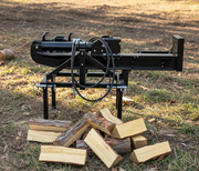 A Paddock Tractor 3pt Mount Log Splitter by Paddock stands on grass outdoors next to freshly split firewood, with trees and sunlight in the background.