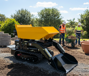 A Paddock Tracked Lifting/Tipping Power Barrow - 800kg Capacity is parked on a construction site, as two workers in safety vests and helmets work near a wheelbarrow and stacked bricks. Trees and a clear sky can be seen in the background.
