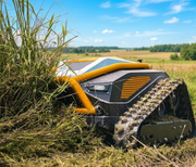 The Paddock™ Remote Controlled Mower 16HP - 740mm by Paddock, equipped with tank-like treads, expertly handles slope mowing and cuts tall grass in a rural field beneath a blue sky with scattered clouds.