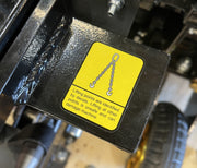 A yellow warning label with a chain symbol on the Paddock Walk Behind Trencher with Guide Wheel warns: Lifting points are marked by decals; lifting elsewhere is unsafe and may damage the machine. A tire is visible in the background.