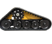 A close-up of the Paddock Tracked Mini Loader Pro by Scintex showcases its yellow track drive system with multiple black wheels and heavy treads, set against a backdrop of shelving and a warehouse floor, ideal for construction uses.