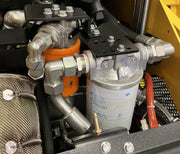 Close-up of a Paddock Tracked Mini Loader Pro’s 40hp Perkins Turbo Diesel engine compartment, showing two orange and white fuel filters, metal pipes, hoses, and connectors among various mechanical components.