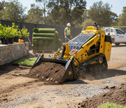 A Paddock Tracked Mini Loader (35hp Kubota diesel, free 4in1 bucket) moves dirt on a landscaping site. In the background, workers in safety vests stand by turf rolls and a white utility vehicle.